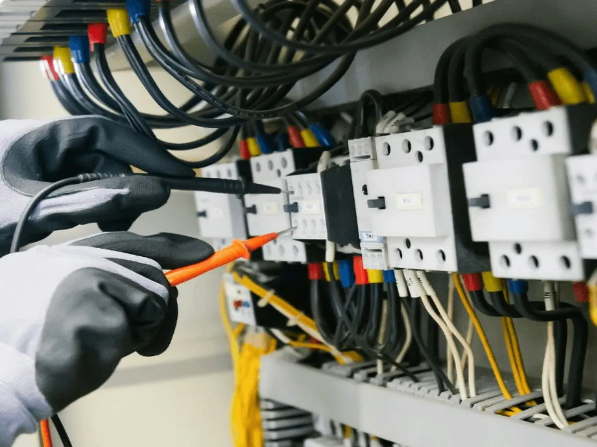 An electrician in work gloves testing an electrical panel with a multimeter